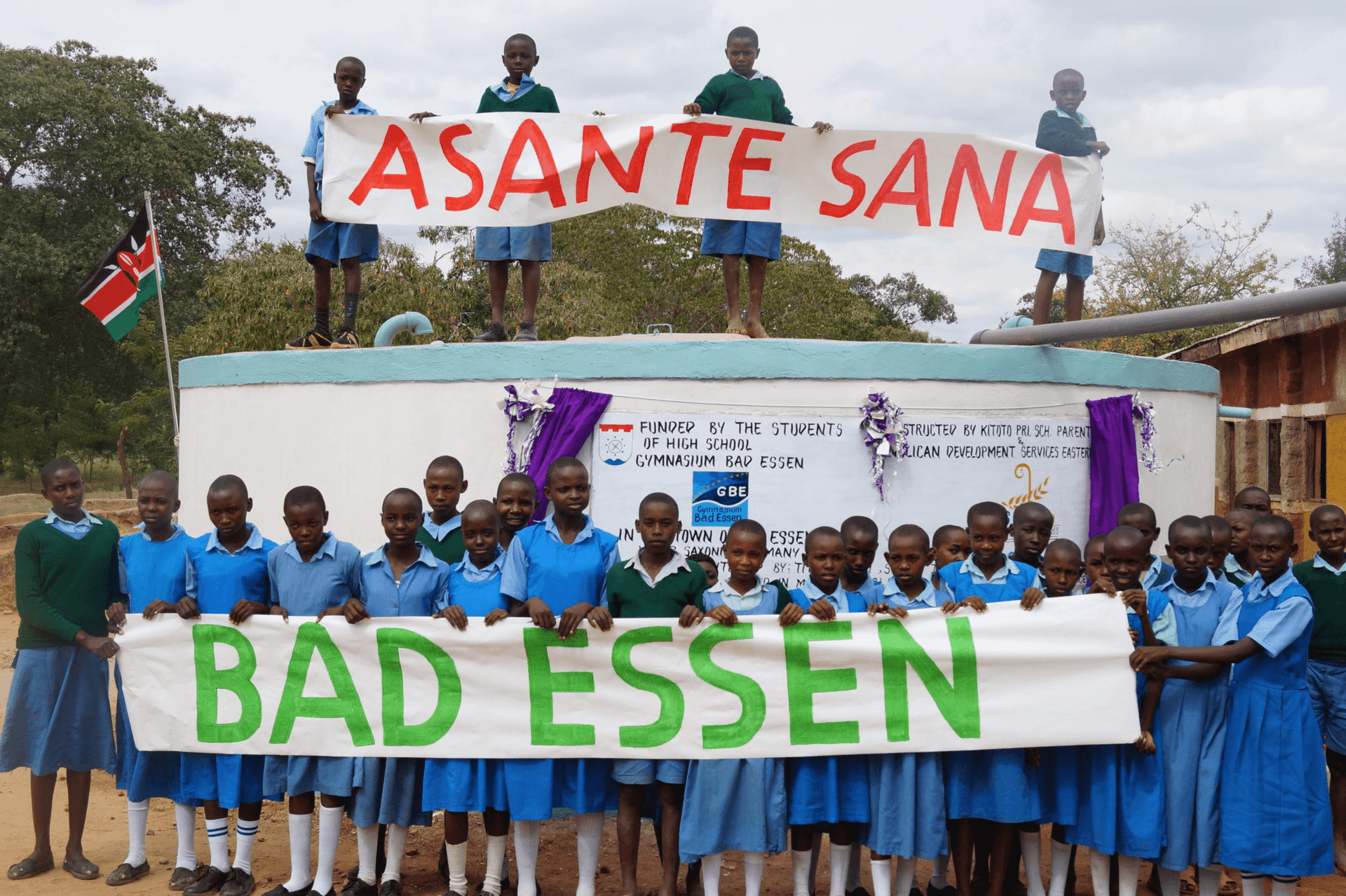 Kinder mit Asante Sana und Bad Essen Banner vor Wasserzisterne