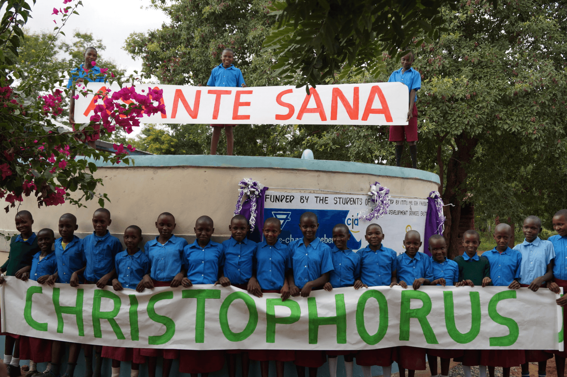 Kinder mit Asante Sana und Christophorus Banner vor Wasserzisterne